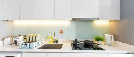 A modern kitchen with white cabinetry, a built-in washing machine, a stovetop, and a coffee maker.