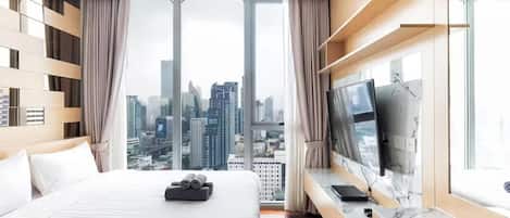 Habitación de hotel con una cama grande, televisión, escritorio y vistas a la ciudad.