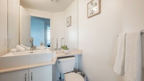 Un baño moderno con un espejo grande, sanitarios blancos, un inodoro y un lavabo.