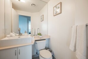 Un baño moderno con un espejo grande, sanitarios blancos, un inodoro y un lavabo.