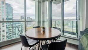 Una habitación moderna con una mesa redonda, cuatro sillas, una planta en maceta y grandes ventanales que ofrecen vistas a la ciudad.