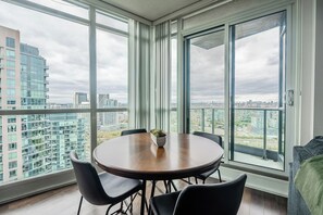 Una habitación moderna con una mesa redonda, cuatro sillas, una planta en maceta y grandes ventanales que ofrecen vistas a la ciudad.