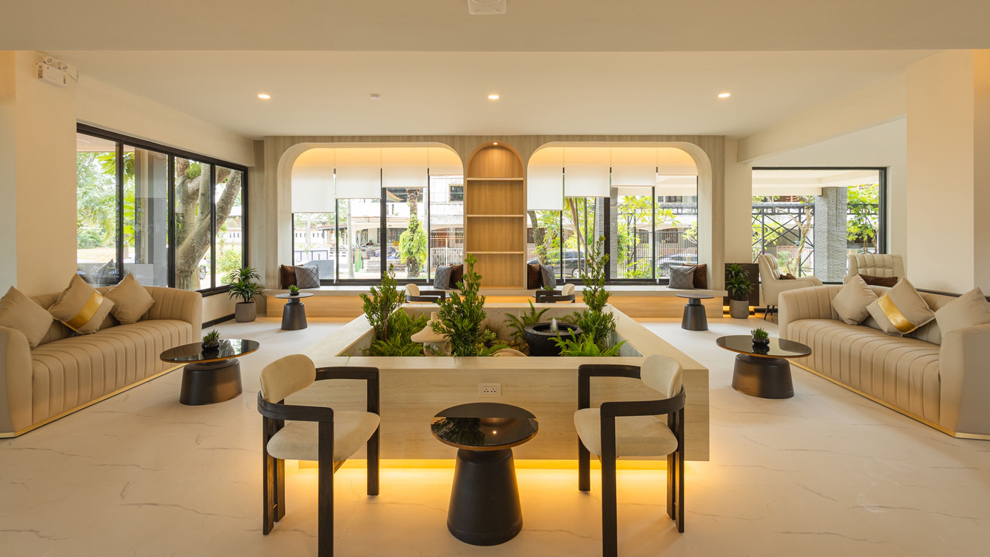 A spacious lounge area with a central coffee table surrounded by chairs, large windows with views of the outside, and a seating area with sofas and a small table.
