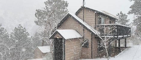 A two-story wooden cabin with a snow-covered roof and a balcony.