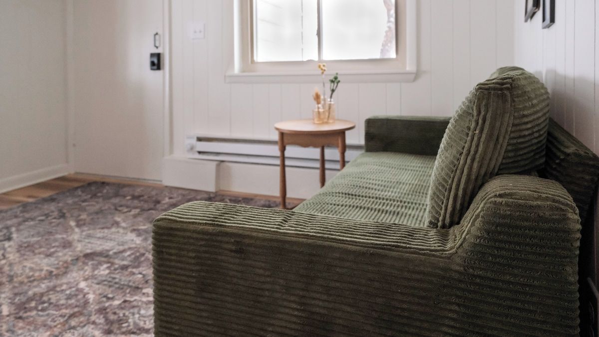 A green sofa with a wooden side table and a vase with flowers.
