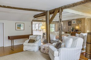 Ein Zimmer mit freiliegenden Holzbalken, einem weißen Sofagarnitur, einer Bank und einem kleinen Tisch mit einer Lampe.