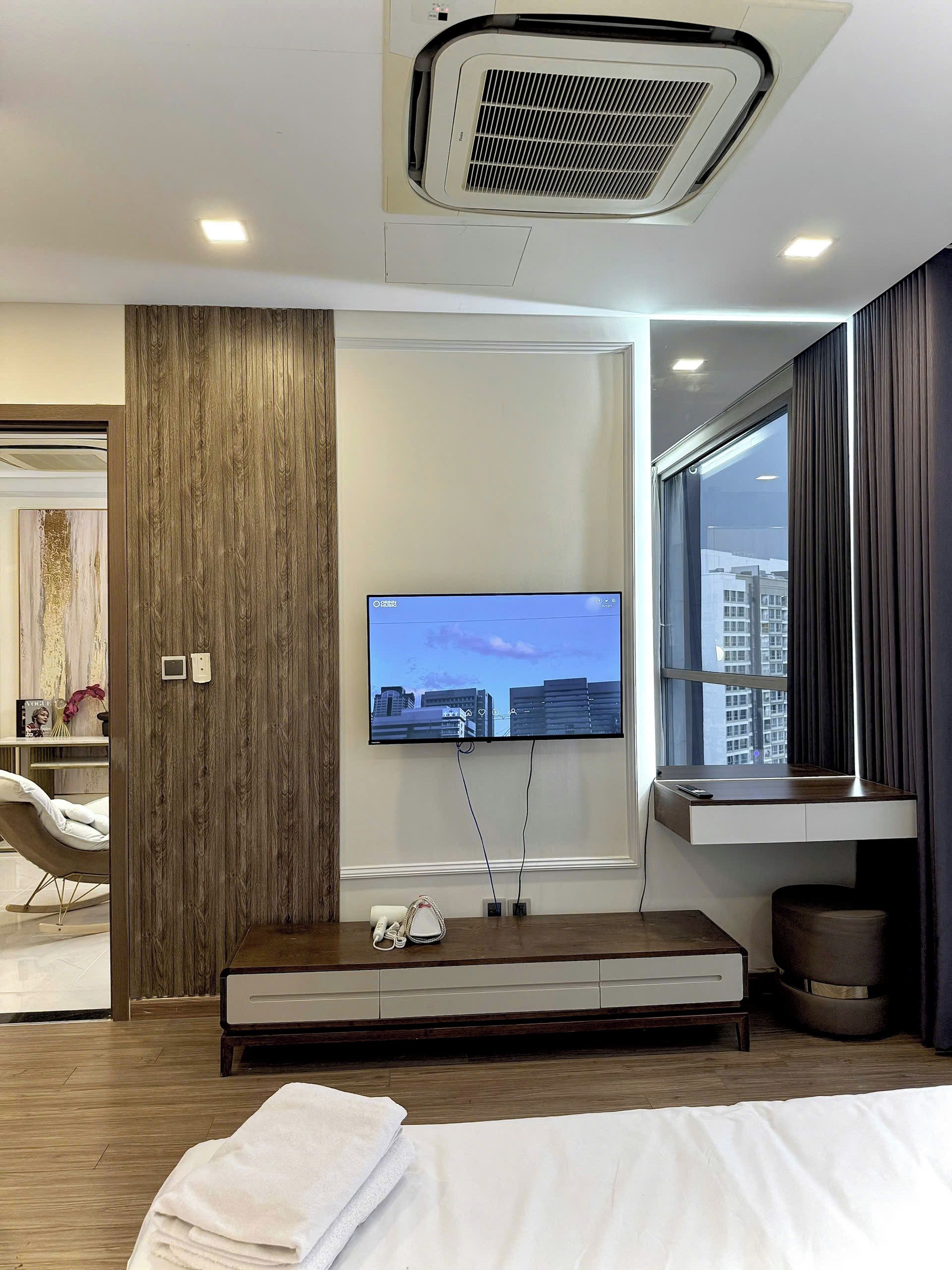Une chambre d’hôtel moderne dotée d’un téléviseur à écran plat fixé au mur, d’un mur d’accent en bois, d’une fenêtre donnant sur des immeubles, d’un bureau avec une chaise et d’un lit agrémenté d’une serviette blanche soigneusement pliée.