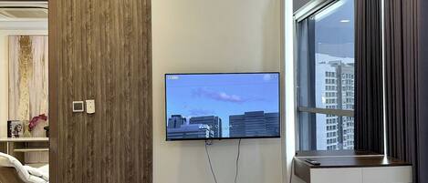 Une chambre d’hôtel moderne dotée d’un téléviseur à écran plat fixé au mur, d’un mur d’accent en bois, d’une fenêtre donnant sur des immeubles, d’un bureau avec une chaise et d’un lit agrémenté d’une serviette blanche soigneusement pliée.