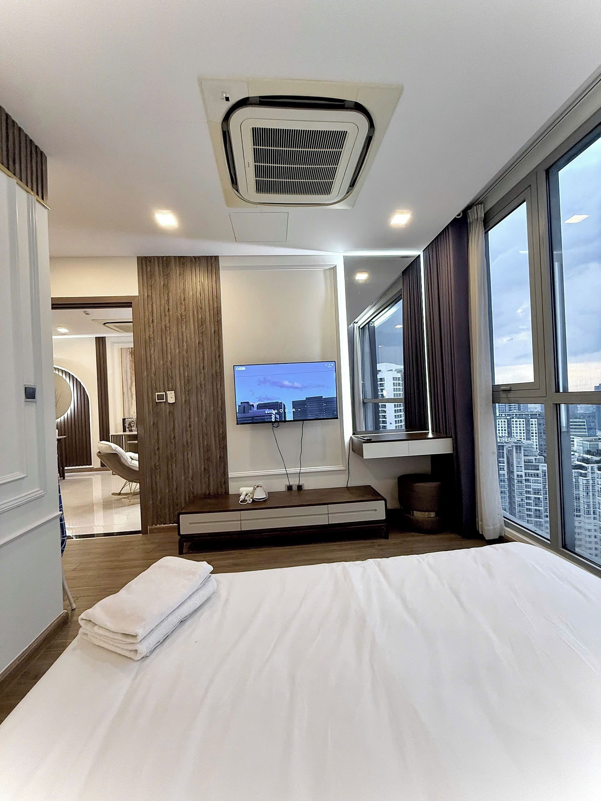 Ein Hotelzimmer mit Bett, Fernseher, Fenster mit Stadtblick und Deckenklimaanlage.