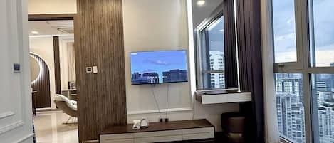 A hotel room with a bed, a TV, a window with a city view, and a ceiling air conditioner.