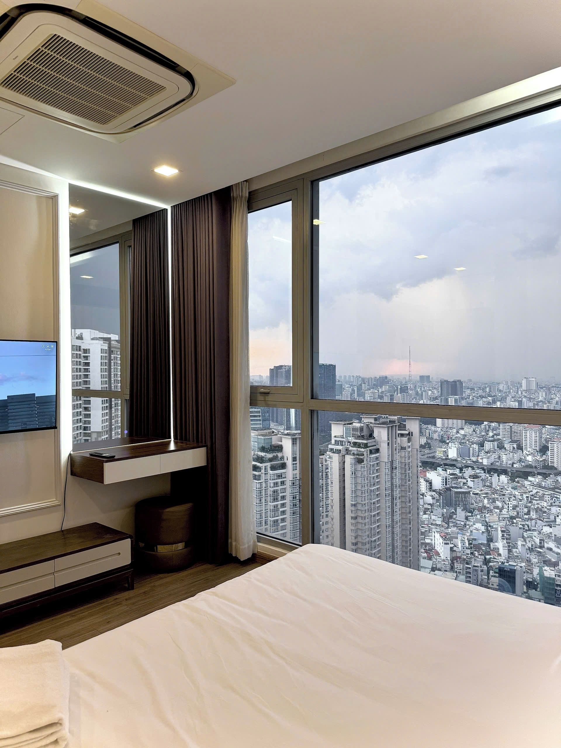 Habitación de hotel con cama, escritorio, televisor y ventana grande con vista a la ciudad.