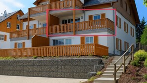A multi-story residential building with balconies, a stone retaining wall, and a staircase leading to the entrance. - Een modern ingericht appartement met een mooi uitzicht over de omgeving (Winterberg)