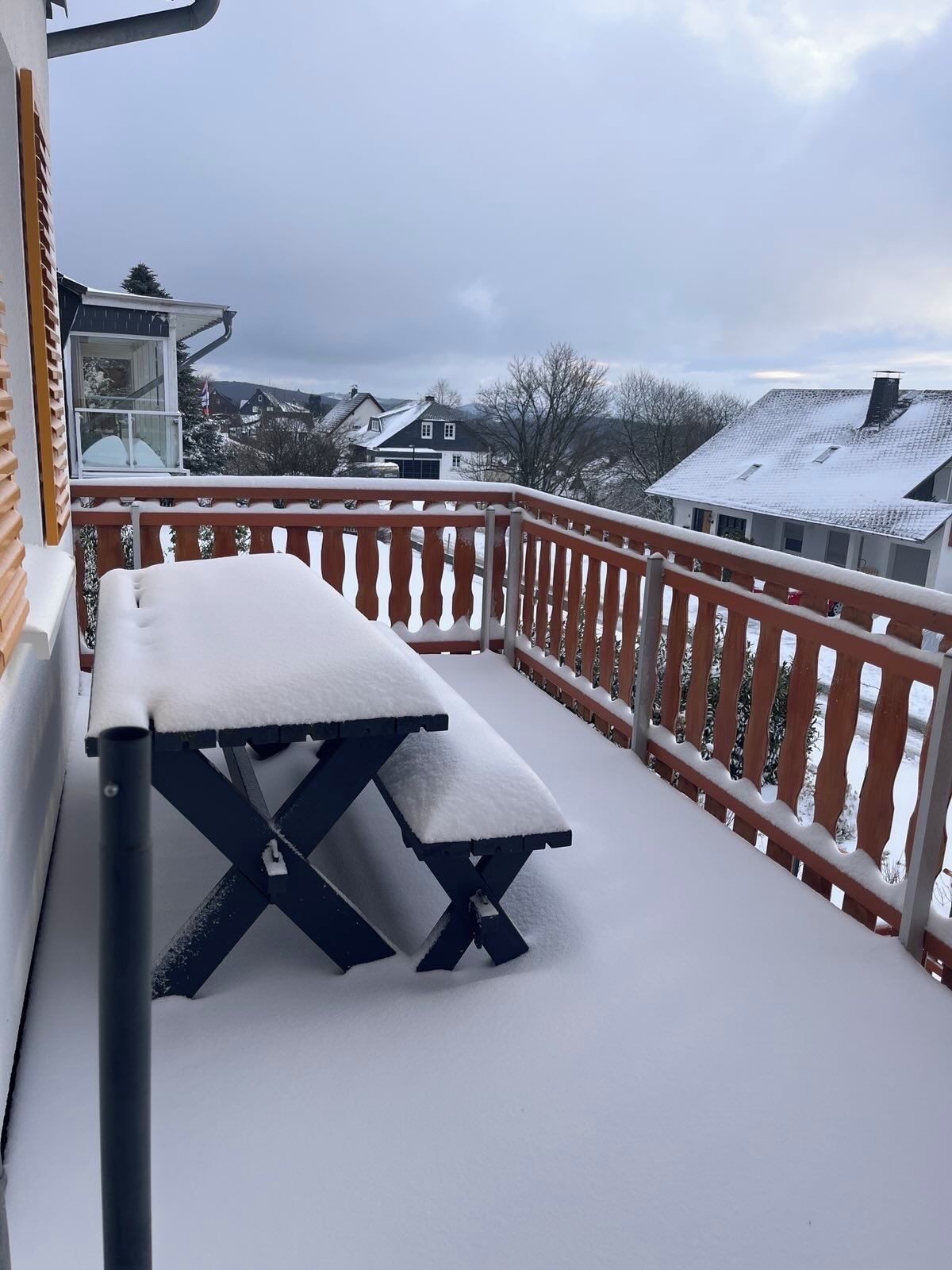 A snow-covered balcony with a picnic table and a railing.