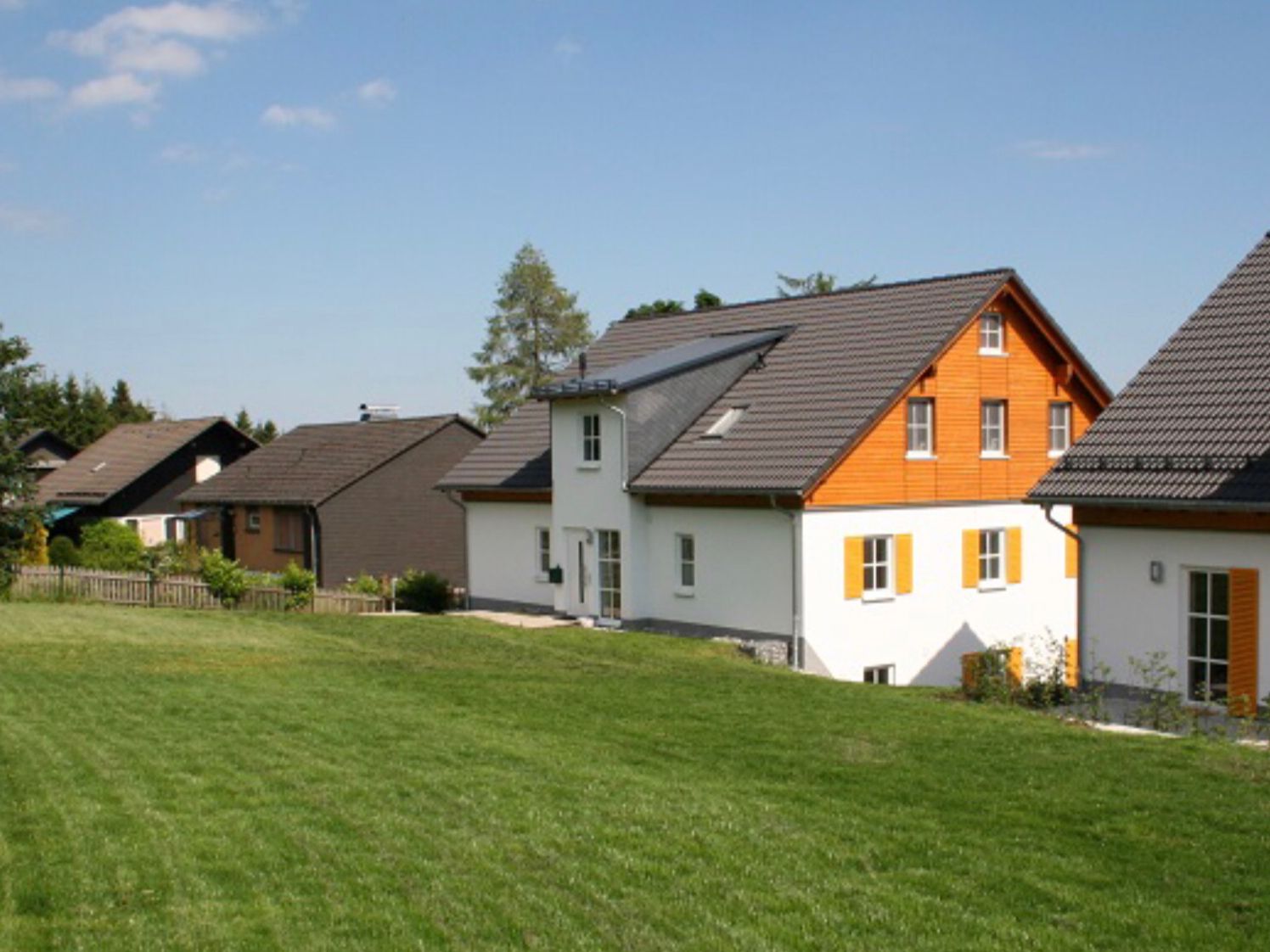 Une rangée de maisons aux toits inclinés, avec une pelouse verdoyante devant et un ciel dégagé.