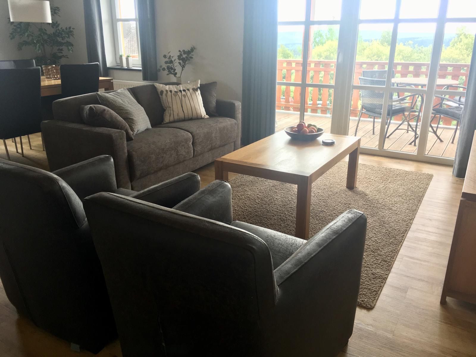 Un salon comprenant un canapé, des fauteuils, une table basse et donnant sur un balcon aménagé avec du mobilier d’extérieur.