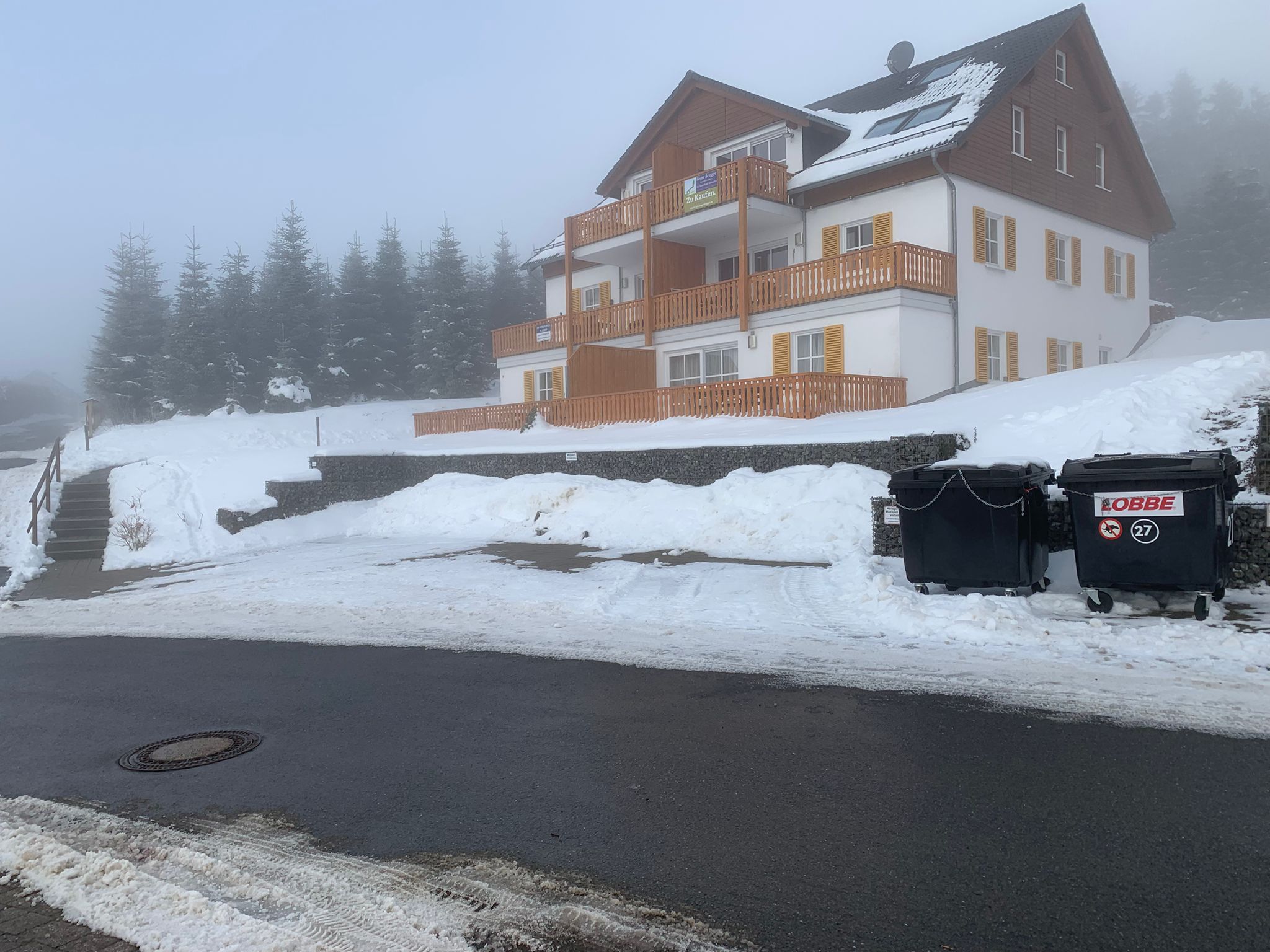Ein zweistöckiges Gebäude mit einem Balkon, einer Steinmauer und einer gepflasterten Straße davor.