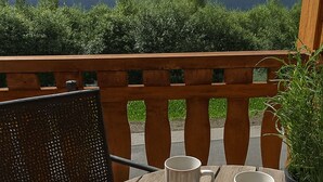 A wooden table with two plates of food and two cups, set on an outdoor deck with a view of trees and hills. - Een modern ingericht appartement met een mooi uitzicht over de omgeving (Winterberg)