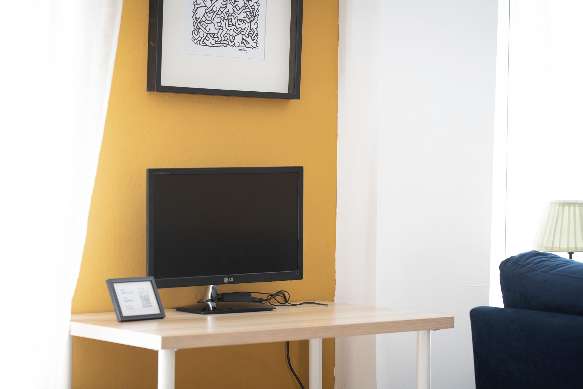 A room with a desk, a computer monitor, a framed picture on the wall, and a blue chair.