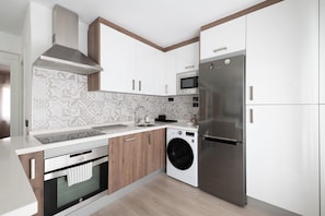 Une cuisine moderne équipée d’un réfrigérateur, d’un four à micro-ondes, d’un four et d’un lave-linge, tous en acier inoxydable.