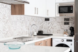 Une cuisine moderne avec des meubles blancs, un four à micro-ondes en acier inoxydable, un lave-vaisselle encastré et des carreaux décoratifs sur le mur derrière l’évier.