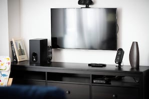 Un téléviseur à écran plat fixé au mur, un haut-parleur noir, une télécommande et un vase décoratif posés sur un meuble de télévision en bois.