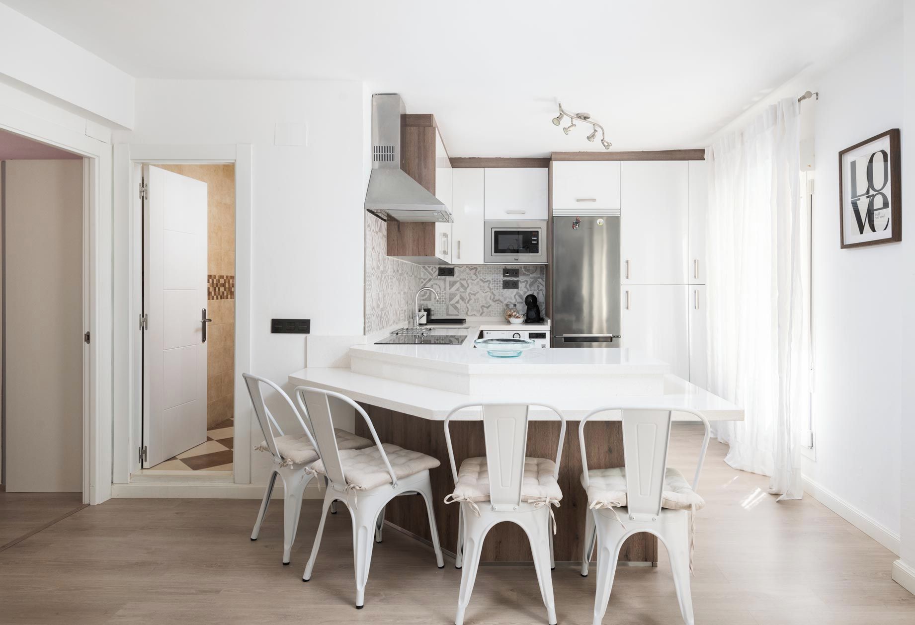Eine moderne Küche mit weißen Schränken, einem Edelstahlkühlschrank und einem Essbereich mit weißem Tisch und Stühlen.