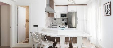 Eine moderne Küche mit weißen Schränken, einem Edelstahlkühlschrank und einem Essbereich mit weißem Tisch und Stühlen.