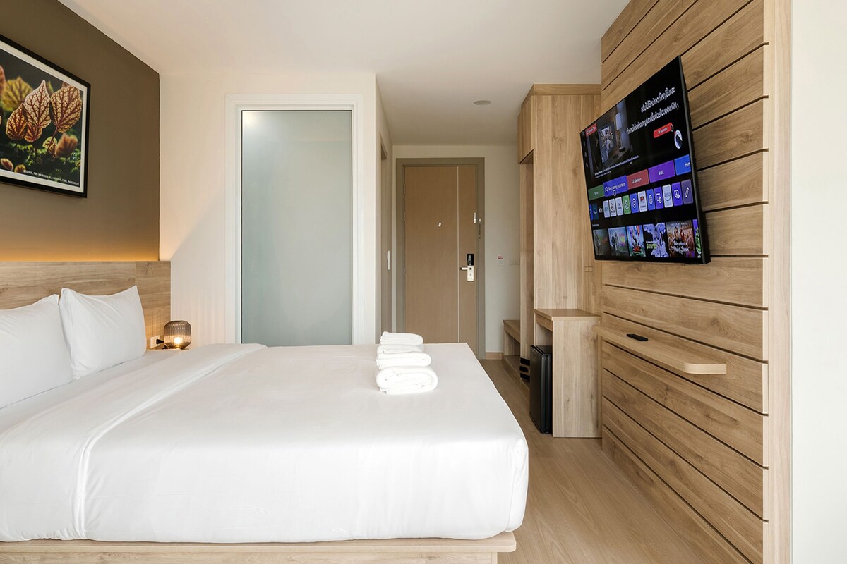 Une chambre d’hôtel avec un lit, un téléviseur fixé au mur et un tableau encadré au-dessus du lit.