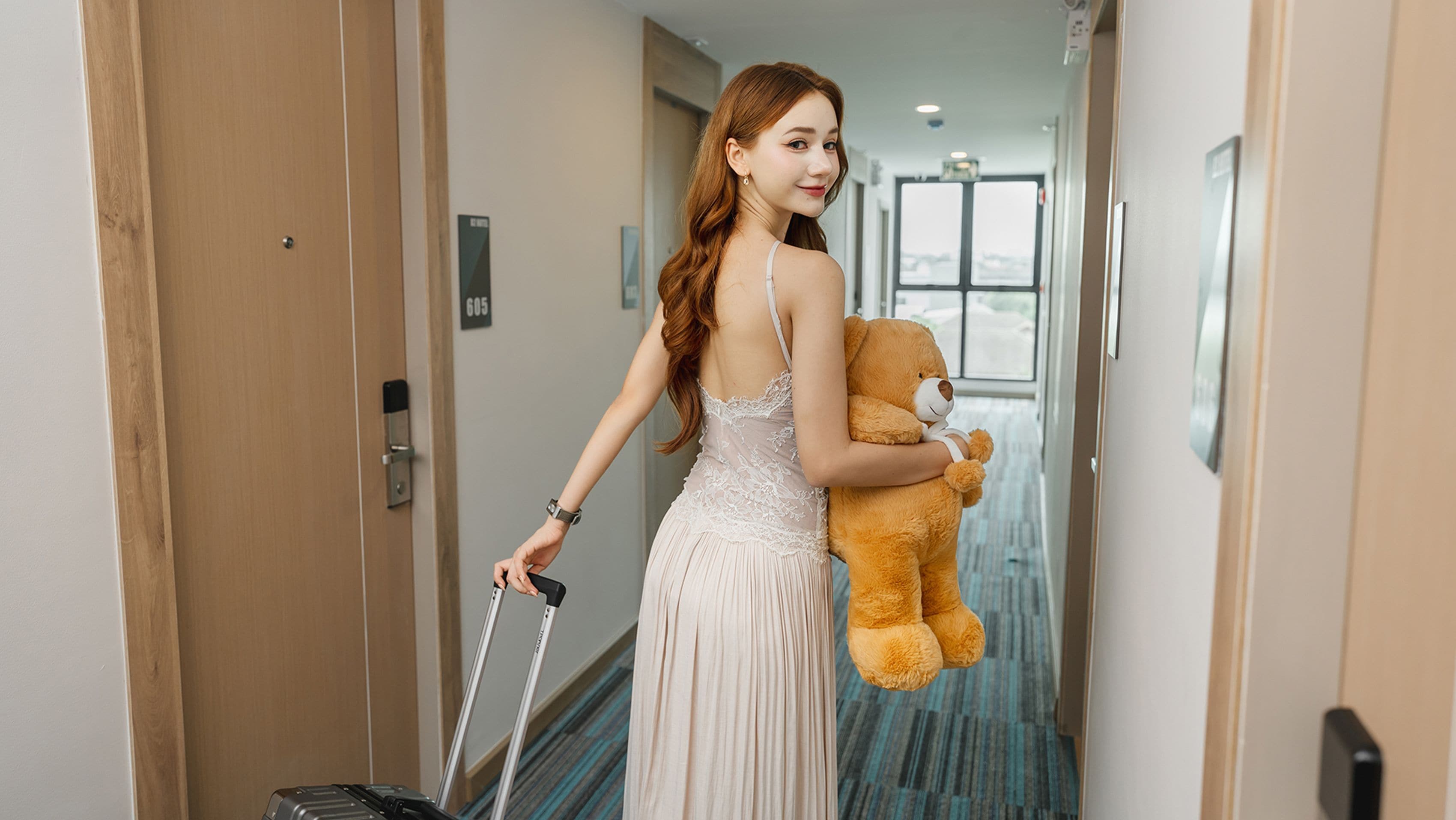 A hotel hallway with a door marked '605', a person holding a teddy bear, and a suitcase.