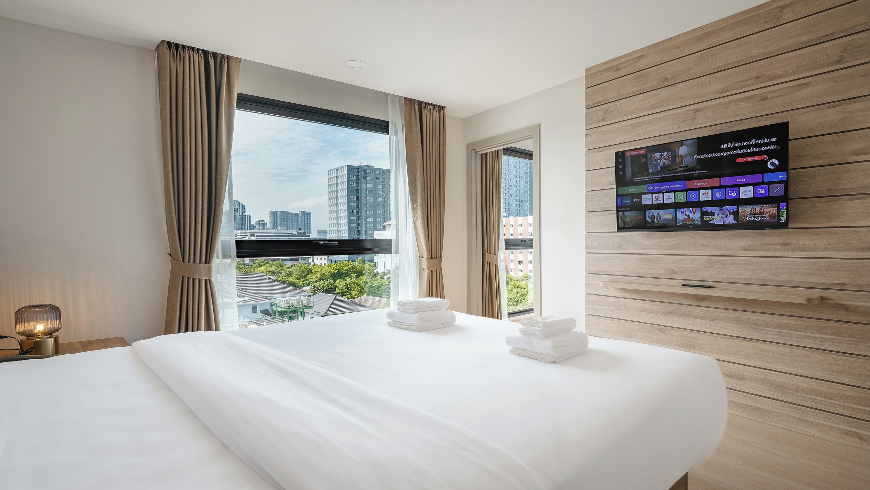 Habitación de hotel con cama, televisor montado en la pared y vista panorámica de la ciudad a través de la ventana.