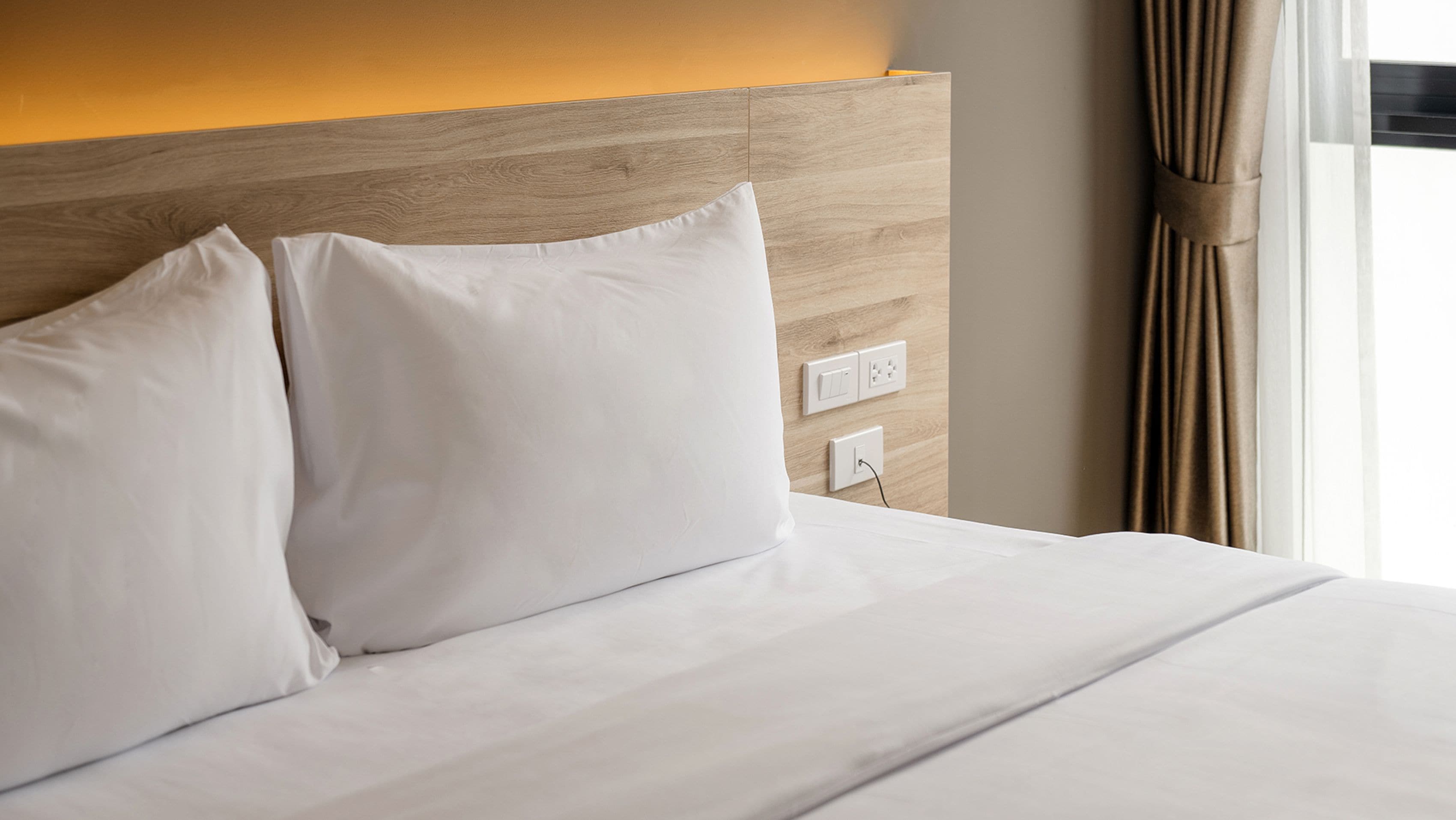 A hotel room with a wooden headboard, white bedding, and a power outlet.