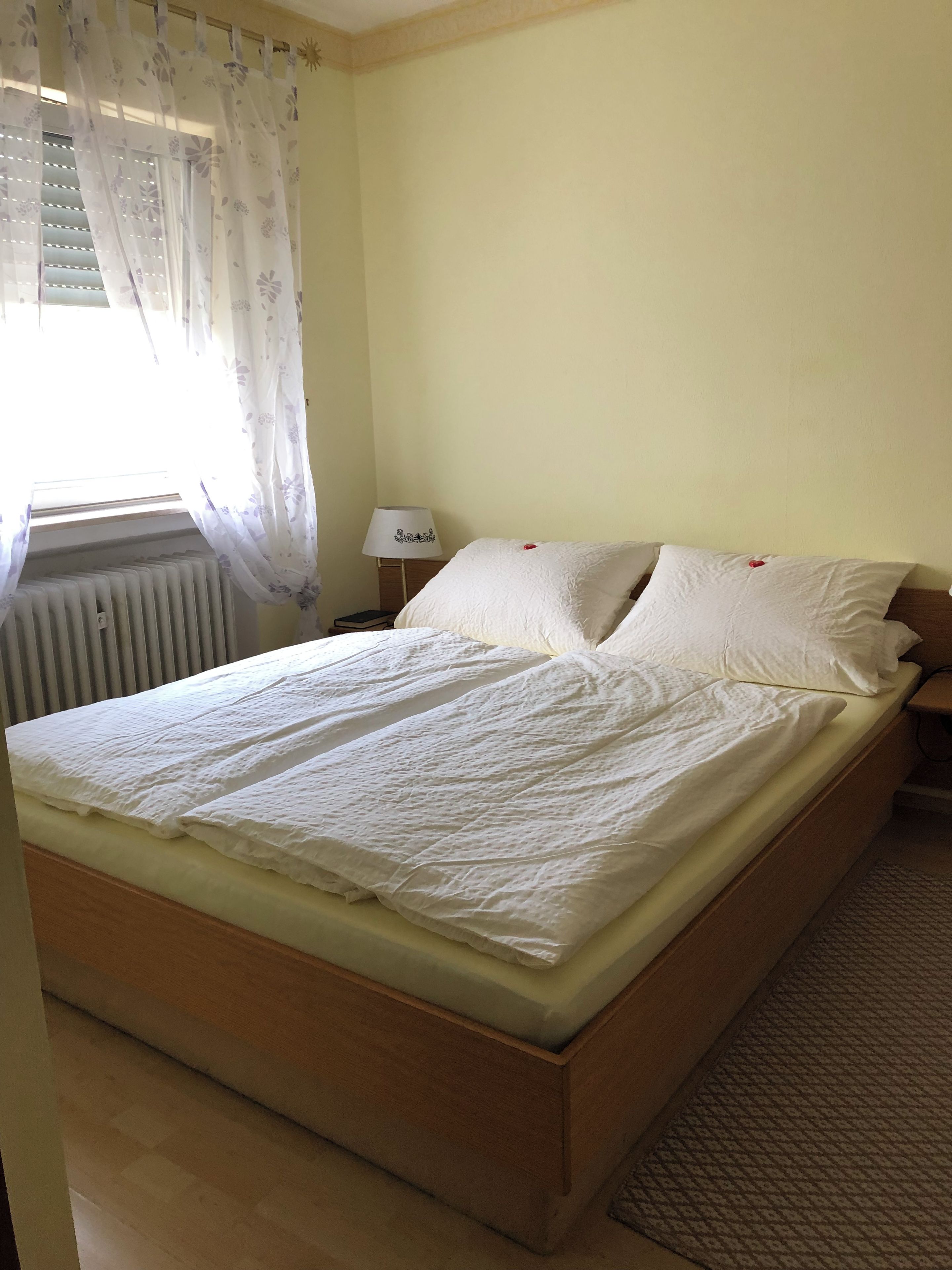Ein Einzelbett mit Holzrahmen, ein Nachttisch mit Lampe und eine Heizung.