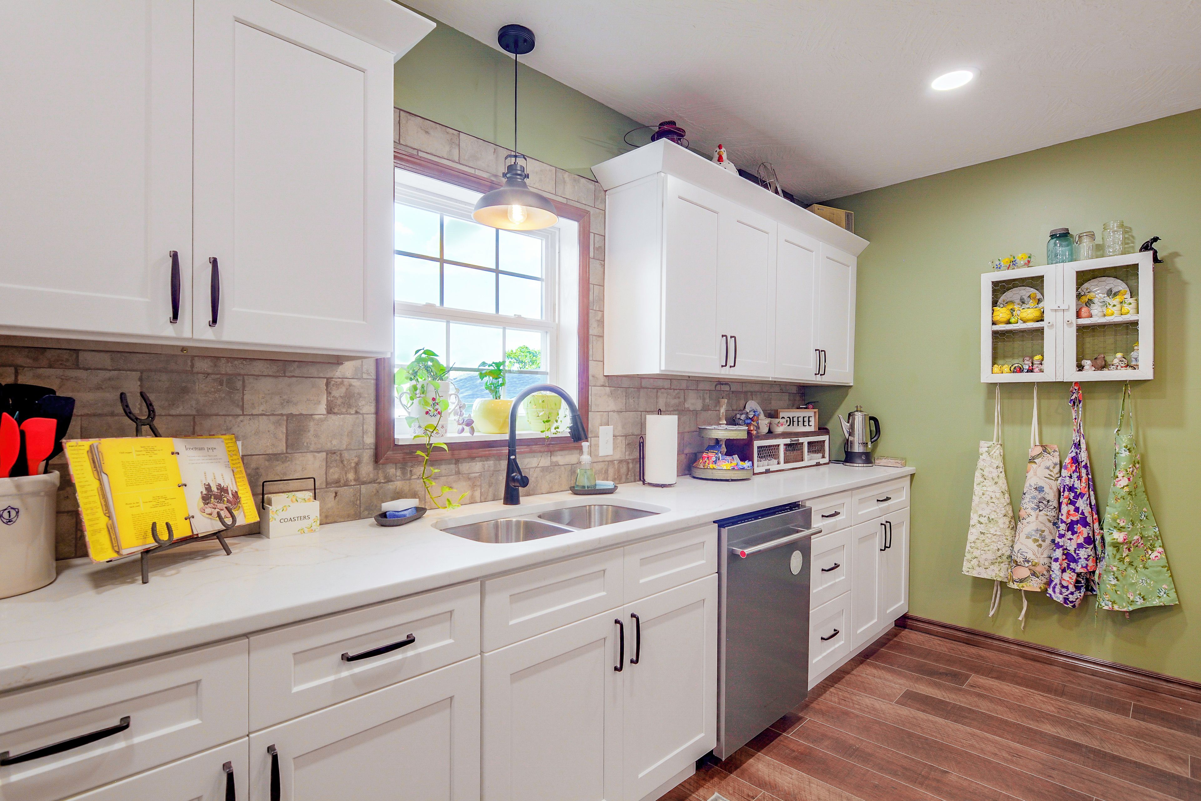 A kitchen with white cabinets, a built-in dishwasher, a window with a view, and a shelf with kitchen items.