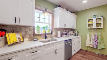 A kitchen with white cabinets, a built-in dishwasher, a window with a view, and a shelf with kitchen items.