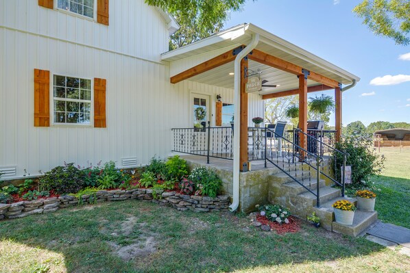 A white building with a covered porch, stone steps, and a garden with various plants.