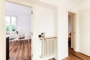 A hallway with a radiator, a door leading to a dining area with a table and chairs, and a view of a window with greenery outside. - Como in the Sky (Como)