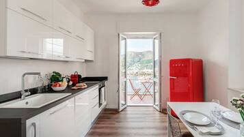 A modern kitchen with white cabinets, a black countertop, and a red refrigerator.