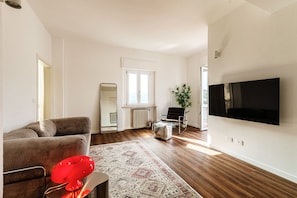 A modern living room with a sofa, a red chair, a large mirror, a potted plant, and a flat-screen TV mounted on the wall. - Como in the Sky (Como)