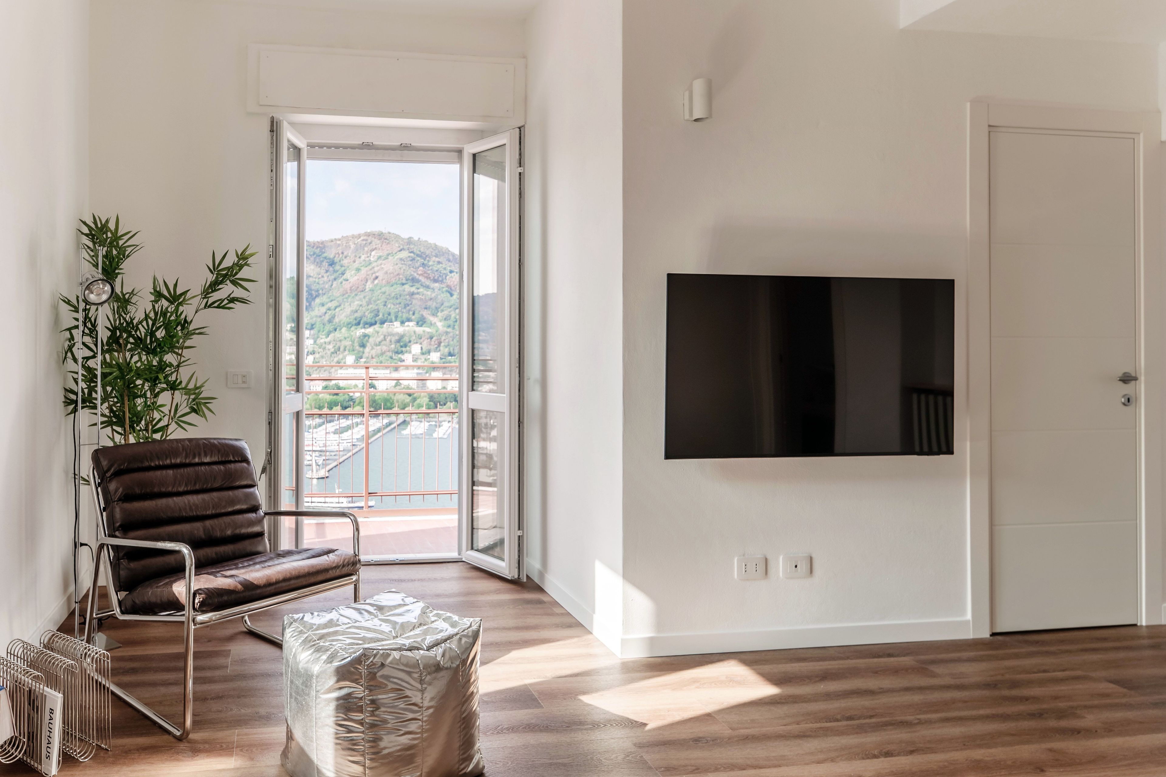 A modern living room with a large TV, a leather chair, a small table, and a view of a cityscape through a glass door.