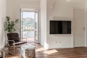 A modern living room with a large TV, a leather chair, a small table, and a view of a cityscape through a glass door. - Como in the Sky (Como)