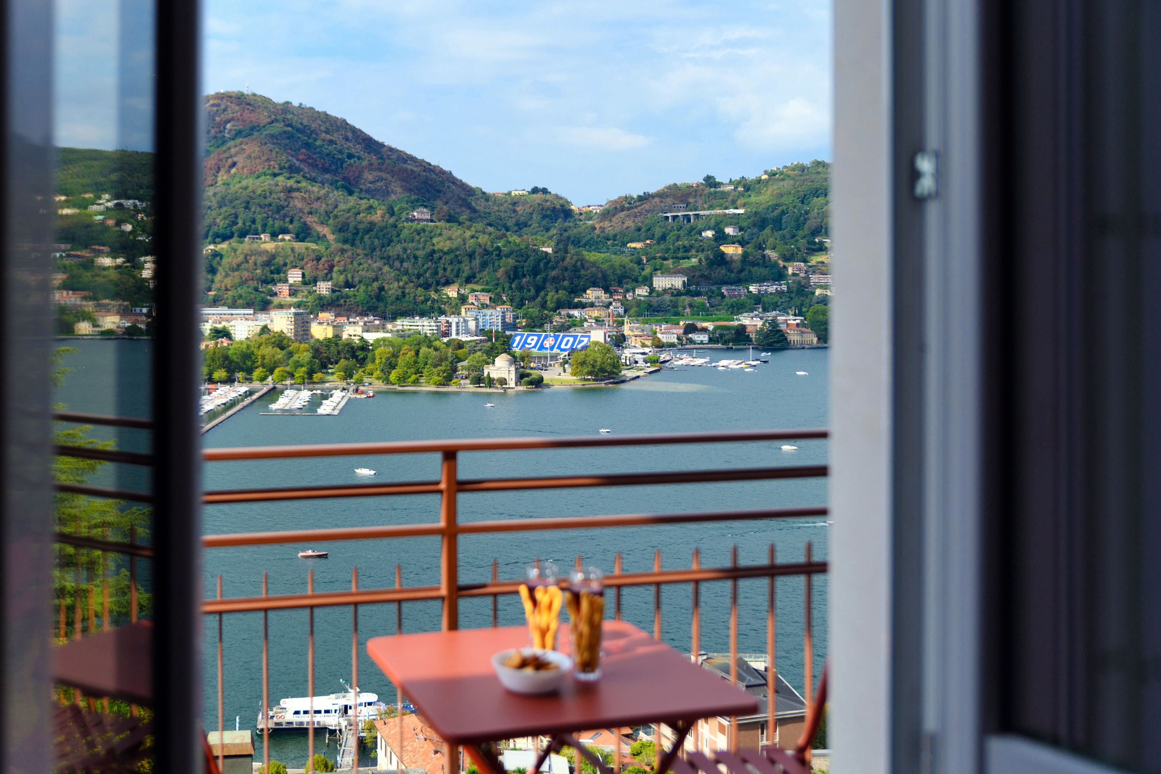 A balcony with a table, a view of a lake, and buildings in the distance.