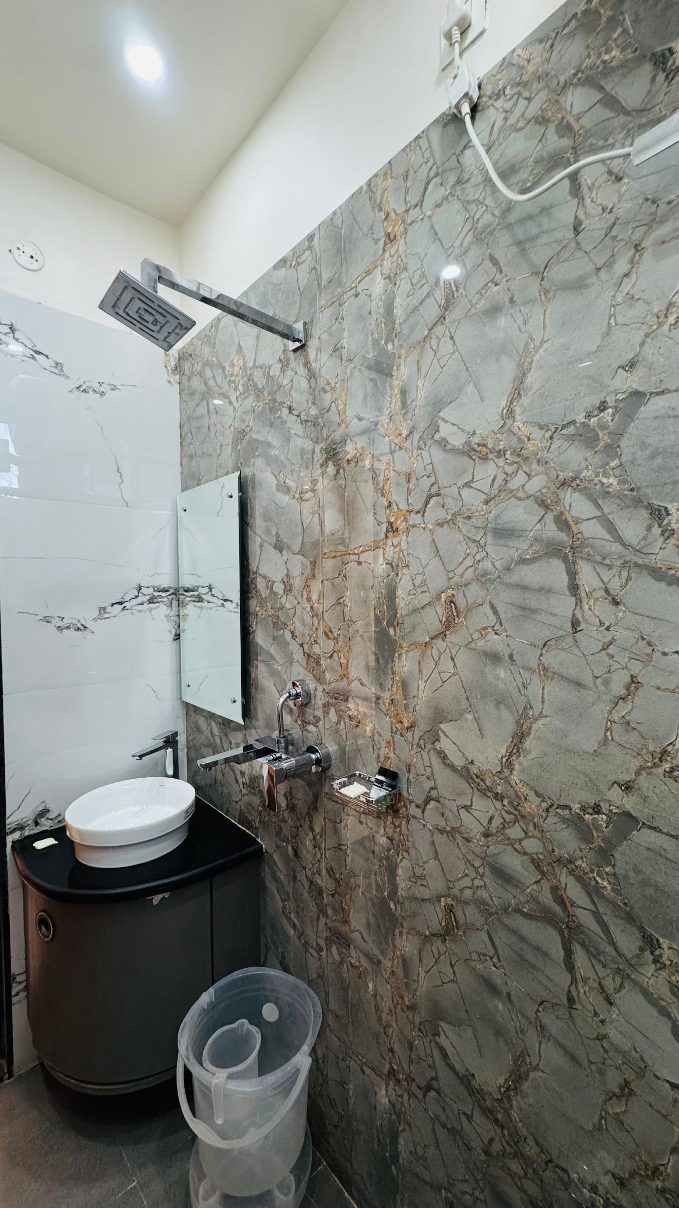 Un baño con pared de mármol, un lavamanos, un espejo y una ducha.