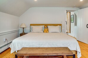 A bedroom with a bed, a bedside lamp, a teddy bear, a wooden bench, and a door. - Walk to Main St! Osterville Cottage w/ Patio (Osterville)
