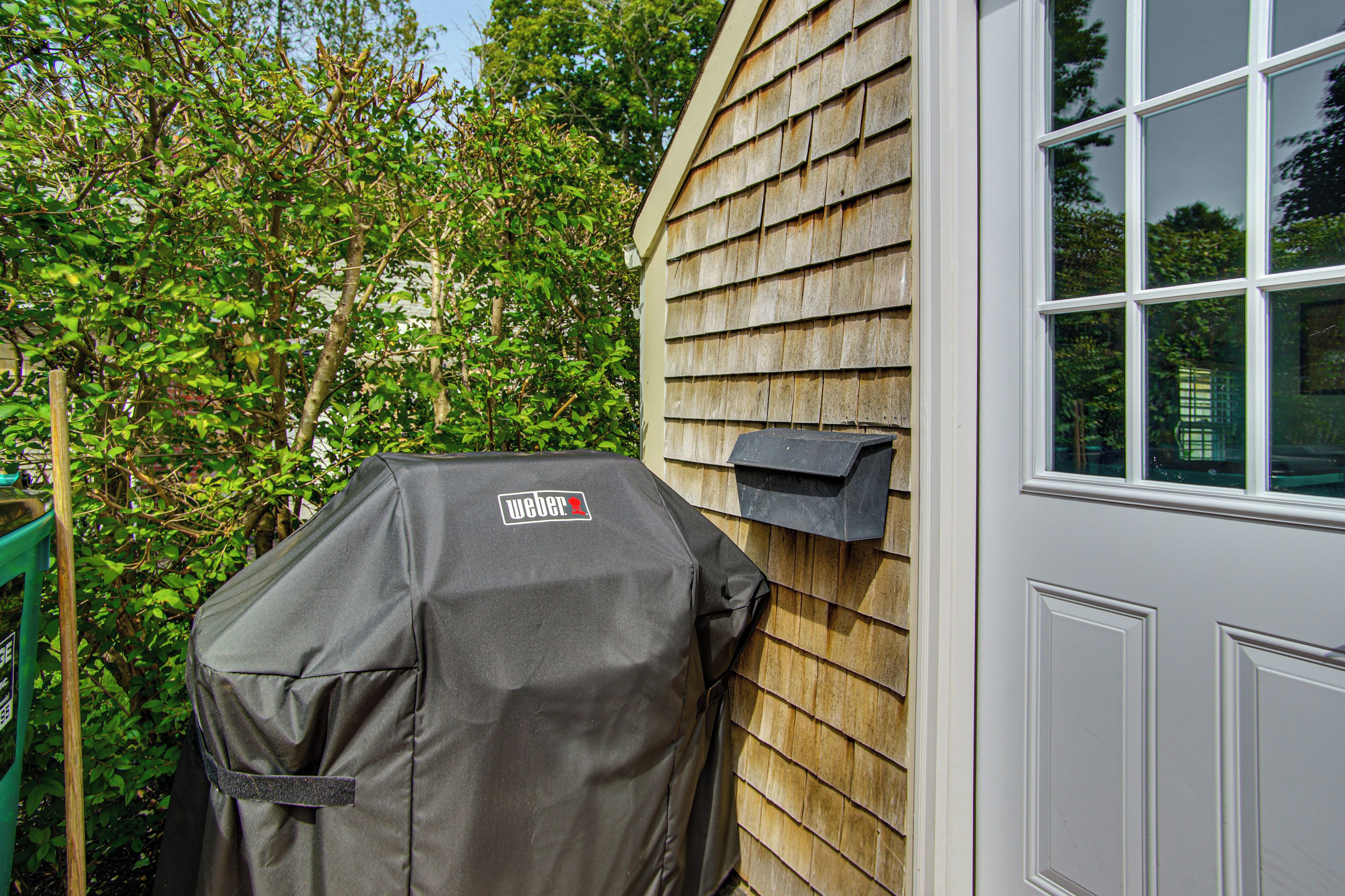 Ein Grill mit Weber-Logo, Holzverkleidung eines Hauses und ein Fenster.