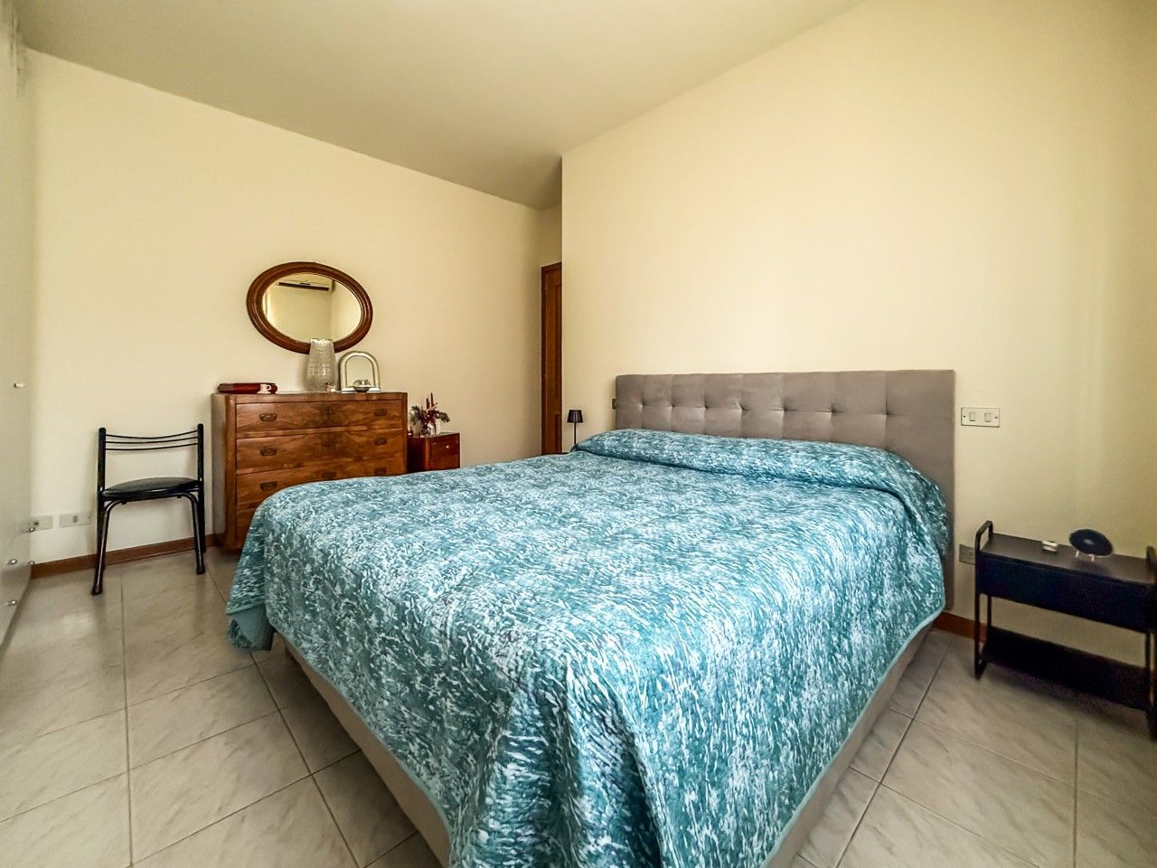 A bedroom with a bed, a dresser, a chair, a bedside table, and a mirror.