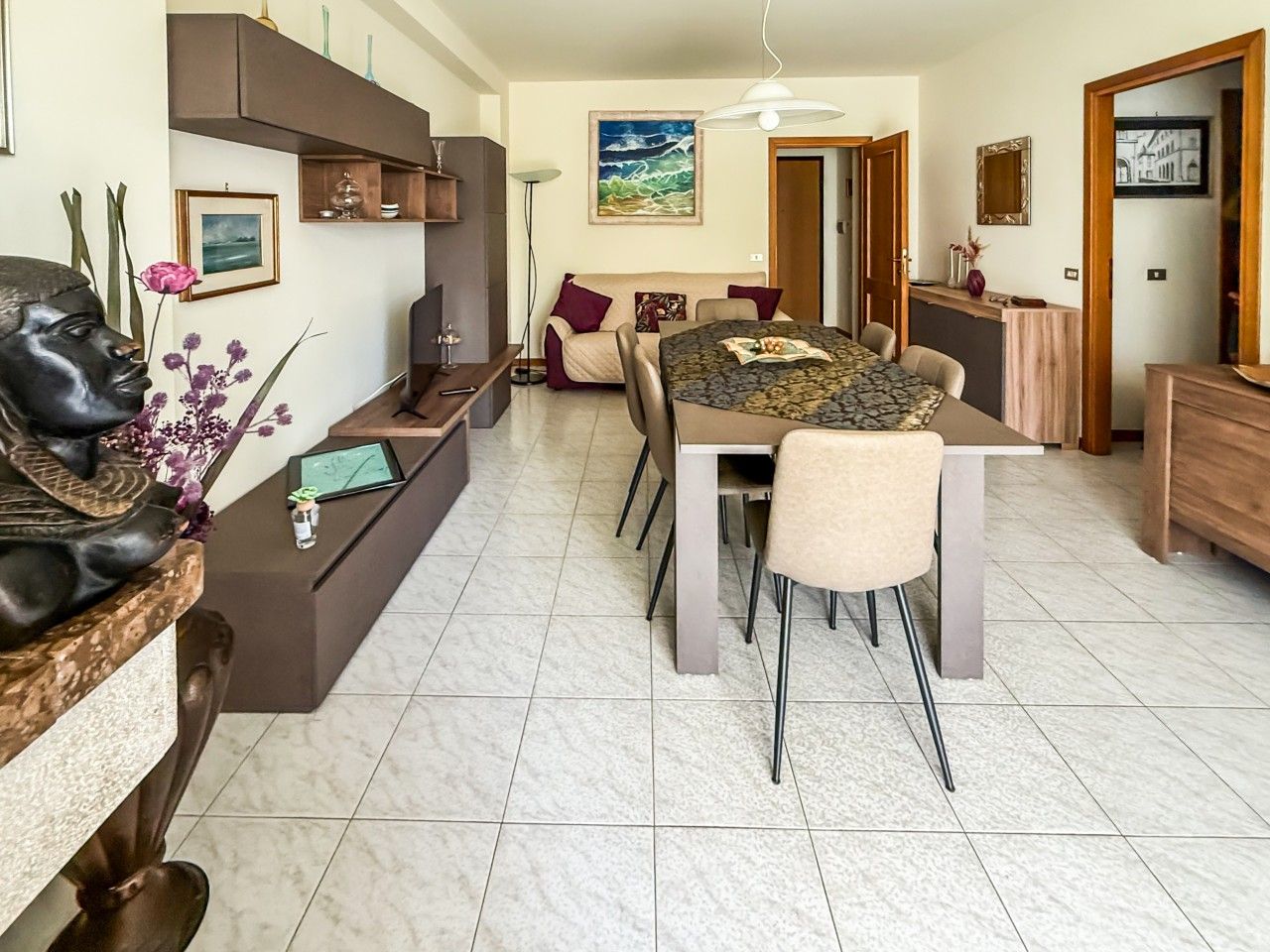 A modern living room with a dining area, featuring a sofa set, a coffee table, and a TV.