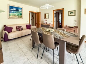 Ein Essbereich mit großem Tisch, Stühlen und einer Couch mit Kissen.