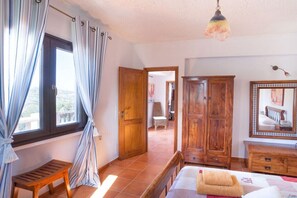 A bedroom with a bed, wooden wardrobe, a bench, a mirror, and a view through an open door. - Villa in Pitsidia with swimming pool (Pitsidia)