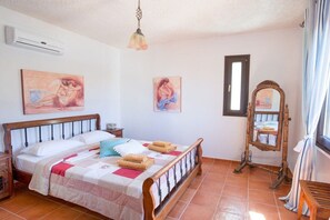 A bedroom with a wooden bed, two paintings, a mirror, and a window with curtains. - Villa in Pitsidia with swimming pool (Pitsidia)