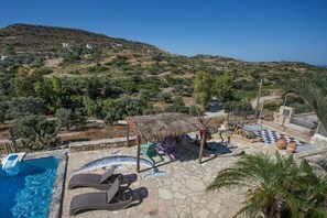 A pool area with lounge chairs, a thatched-roof structure, and a view of a hilly landscape. - Villa in Pitsidia with swimming pool (Pitsidia)
